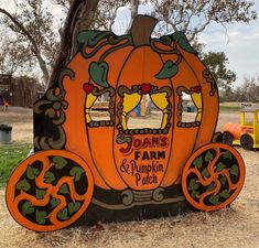 an orange and black pumpkin shaped sign sitting under a tree