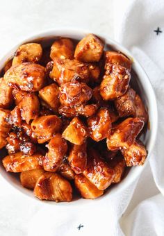 a white bowl filled with chicken and sauce on top of a table next to a napkin