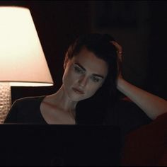 a woman sitting in front of a laptop computer on a table next to a lamp