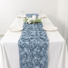 the table is set with white plates and silverware on it, along with blue runneres