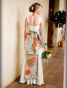 a woman standing in front of a wall wearing a dress with flower designs on it