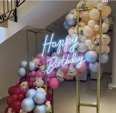 a happy birthday sign surrounded by balloons and flowers on display in a room with stairs