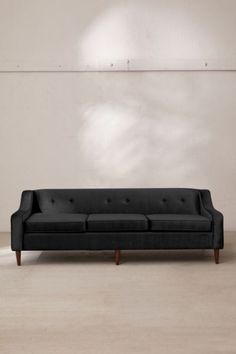 a black couch sitting on top of a hard wood floor next to a white wall