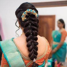 a woman with long hair in a braid wearing an orange and blue saree, looking at herself in the mirror