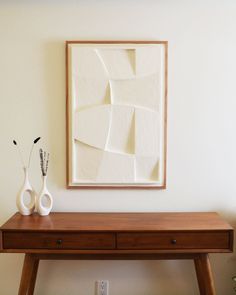 two white vases sitting on top of a wooden table in front of a painting