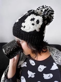 a woman drinking from a cup while wearing a black and white hat with skulls on it