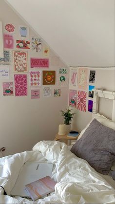 a white bed topped with lots of pillows next to a wall covered in pictures and posters