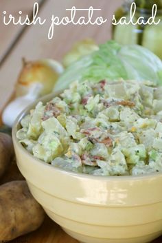 a bowl filled with potato salad sitting on top of a wooden table next to vegetables