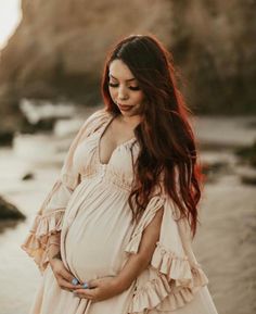 a pregnant woman standing on the beach with her belly in her hands and looking down