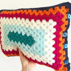 a crocheted pillow is held up to show the colorful stitchs on it