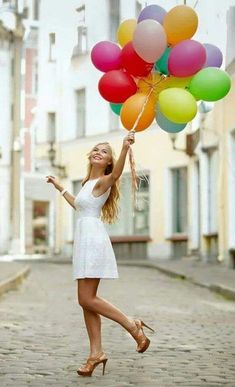 a woman in a white dress is holding some colorful balloons and posing for the camera