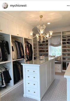 a walk in closet filled with lots of white cabinets and drawers next to a chandelier