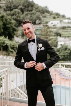 a man in a tuxedo smiles while standing next to a pool and fence