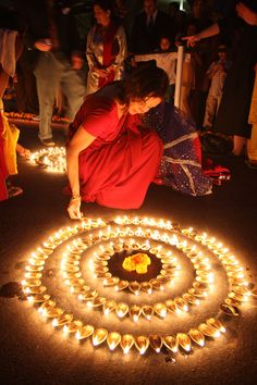 a woman kneeling down on the ground in front of a circle of candles with people standing around