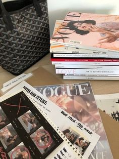 several magazines are stacked on top of each other next to a purse and handbag