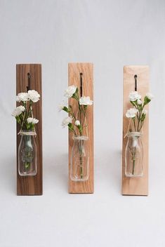 three glass vases with flowers in them are on wooden stands, one is hanging from the wall