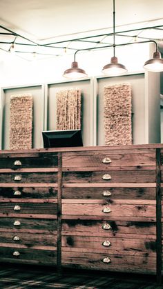 a wooden dresser sitting inside of a room next to two light shades on the ceiling