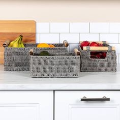 two wicker baskets filled with fruit on top of a white countertop next to a cutting board