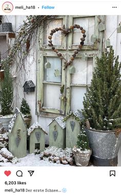 an old window is covered in snow and decorated with small christmas trees, potted plants and wreaths