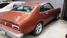 an orange muscle car parked in front of a garage with two other cars behind it