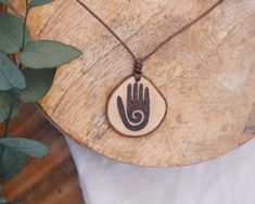 A handmade boho necklace with an engraved hand made from local hardwood. Since I make each piece of jewelry by hand and each piece of wood is unique, your delivered necklace may vary slightly from the product images. I hand burn the design into the wood and treat it with natural oil. The oil protects the pendant from external influences and keeps it looking beautiful for a long time. Nevertheless, the chain should be removed before showering or swimming. The pendant is attached to a waxed cotton cord with adjustable length. So the length of the necklace can be varied. The pendant has a diameter of about 3 cm. Each piece of my shop is from fallen tree limb, so no trees are ever damaged.  Visit my shop to find more hippie and festival jewelry! Vegan product. Handmade with love. Plastic-free Wood Burned Necklace, Adjustable Bohemian Wood Jewelry, Handmade Artisan Wood Jewelry, Handmade Adjustable Wood Jewelry, Artisan Handmade Wooden Jewelry, Natural Wooden Bohemian Jewelry, Natural Wood Bohemian Jewelry, Handmade Natural Wood Pendant Jewelry, Handmade Wooden Pendant Jewelry