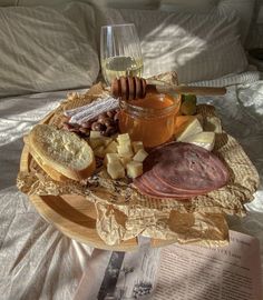 a plate with bread, cheese, ham and honey on it next to a glass of wine