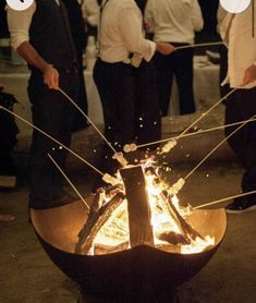 a group of people standing around a fire pit with sticks sticking out of it's sides