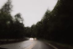 the windshield of a car with trees in the back ground and raindrops on it