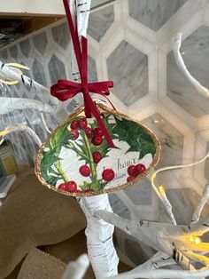 a christmas ornament hanging from the side of a tree with holly and berries on it