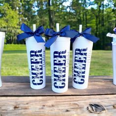 three white tumblers with blue bows and the words cheer on them are sitting on a picnic table