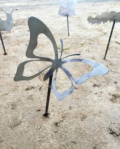 three metal butterflies are standing in the sand