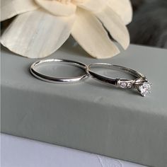 two wedding rings sitting on top of a table next to a flower and white petals