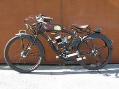 an old fashioned motorcycle parked next to a brown wall with metal parts on the front wheel