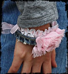 a person wearing a pink bracelet with lace on it's wrist and holding onto a pair of jeans