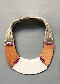 This striking handmade necklace is a bold fusion of modern design and natural materials. Its centerpiece is crafted from laser-cut white acrylic, creating a sleek, smooth, and contemporary look. The acrylic is beautifully complemented by a wooden element, adding warmth and texture, which is bound together with delicate pink laces for a soft, playful contrast. The strap is an elegant combination of 100% genuine silver leather, lending a luxurious metallic sheen, and thick fabric laces in a soft b Unique Enamel Inlay Necklaces, Luxury Handmade Modernist Necklace, Luxury Modernist Gold Necklace, Modernist Metal Necklace With Polished Finish, Collectible Modernist Pendant Necklace, Polymer Crafts, Pink Lace, White Acrylics, Wedding Jewellery Necklace