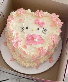 a hello kitty cake in a box with pink flowers on the bottom and white frosting