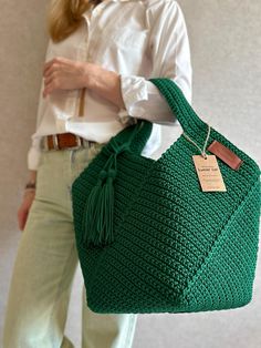 a woman holding a green crocheted bag with a tag on it's handle