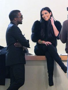 a woman sitting on top of a counter next to a man in a black suit