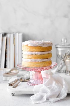 a frosted cake sitting on top of a glass plate next to books and silverware