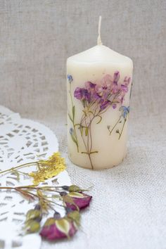 a white candle sitting on top of a table next to a doily and flowers