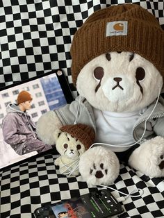 a teddy bear sitting on top of a black and white checkered table cloth next to a cell phone