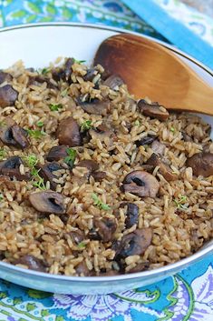 a bowl filled with rice and mushrooms on top of a blue table cloth next to a wooden spoon