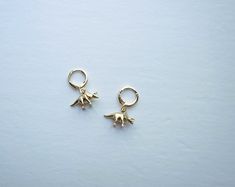 "*Dainty, fun, cute and charming Triceratops huggie hoop earrings! I love dinosaurs and I know you do too! *Layer with other hoops/earrings or wear on its own. *Gold plated over brass Triceratops dinosaur charm, 18x11mm *18k Gold plated 12mm leverback huggie hoops *Quality, small batch, unique, chic *Makes a great gift for a friend or family member...or for yourself! *3 other kinds of dino earrings in the shop! Check them out! *Won't tarnish easily but please take care of your jewelry! Please re Dainty Small Hoop Earrings With Charms, Dainty Green Huggie Hoop Earrings, Dainty Green Hoop Earrings, Dino Nugget Earrings, Dino Earrings Gold, Gold Dinosaur Earrings, Dinosaur Earrings, Huggie Hoop Earrings, Raw Brass