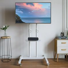 a flat screen tv sitting on top of a white stand next to a wooden table