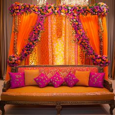 an orange couch with pink and yellow pillows in front of a stage decorated with flowers