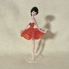 a glass figurine with a red dress and black hair is standing on a white surface