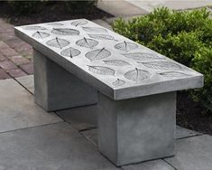 a concrete bench sitting on top of a sidewalk next to bushes and shrubbery with leaves drawn on it