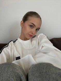 a woman sitting on top of a couch wearing sweatpants and a white sweatshirt with black stripes