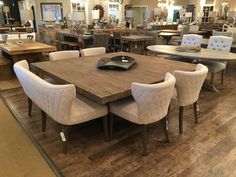 a large dining room table surrounded by white chairs and wooden tables in the middle of an open floor plan