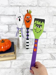 three halloween spoons with faces painted on them, one being held by a hand